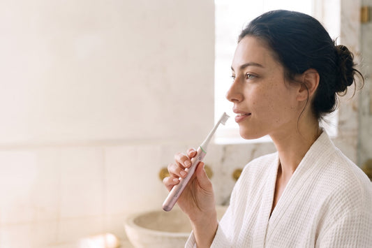 Woman brushing gently with a Rose PulseONE sonic toothbrush in a sunlit bathroom
