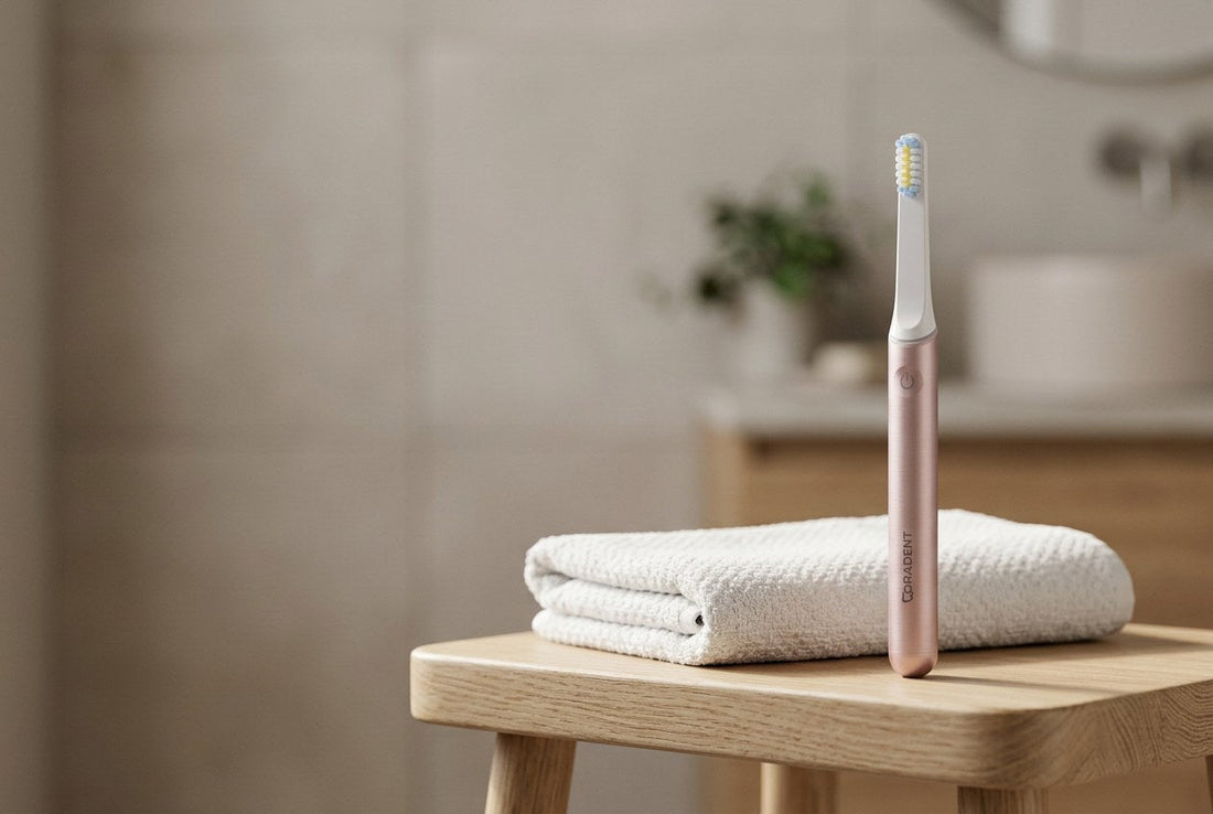 PulseONE sonic toothbrush in Rose standing on a light timber bathroom stool beside a neatly folded white towel