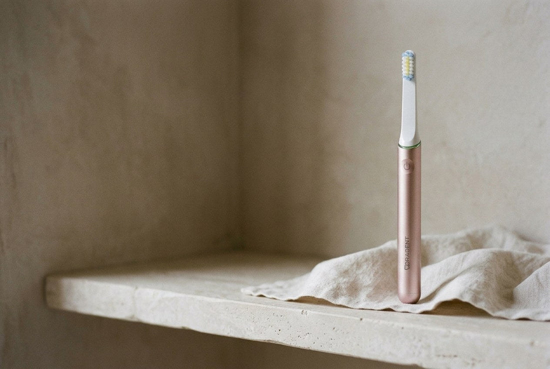 PulseONE sonic toothbrush in Rose standing on a soft white linen cloth on a pale stone shelf