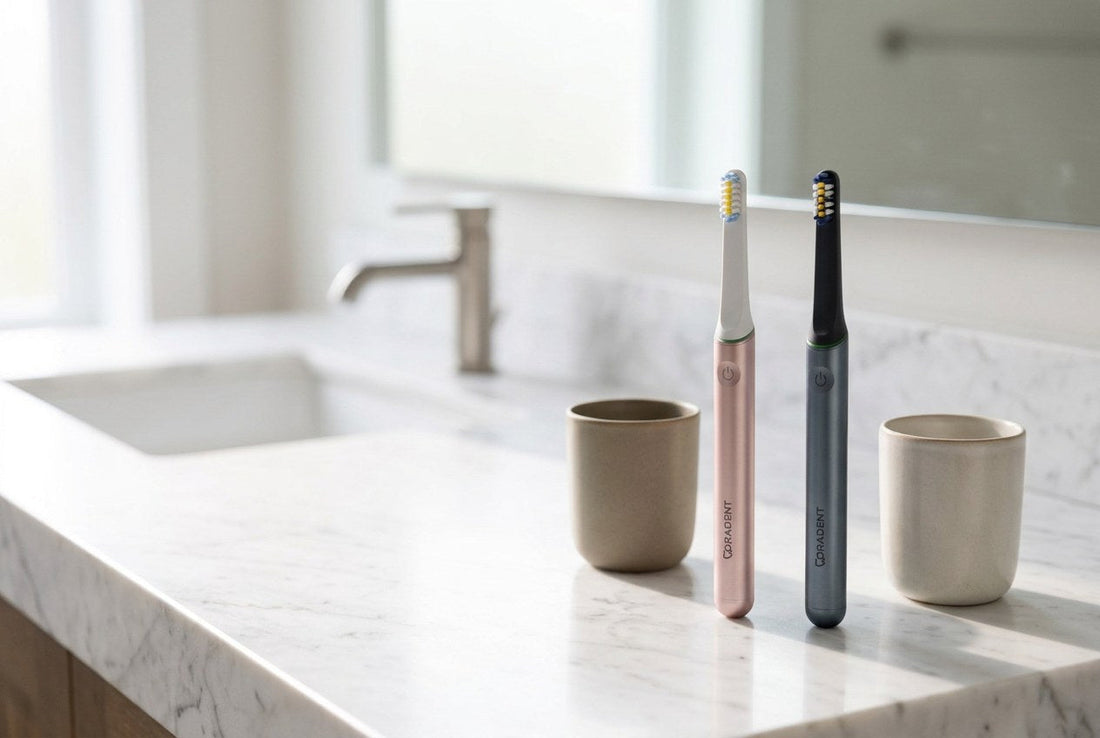 Two PulseONE sonic toothbrushes in Rose and Graphite on a pale travertine bathroom ledge with a folded linen towel