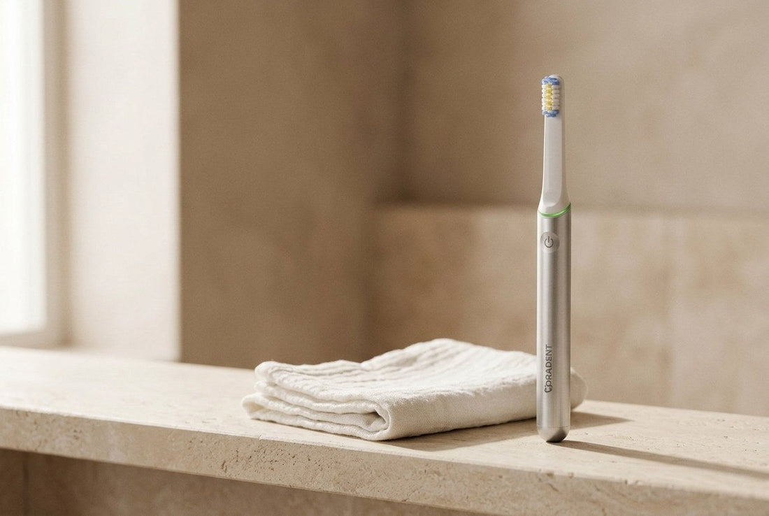 PulseONE sonic toothbrush in Platinum on a pale stone bathroom shelf beside a folded white cotton cloth