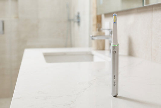PulseONE sonic toothbrush in Platinum standing on a clean white quartz surface in a bright modern clinic style bathroom