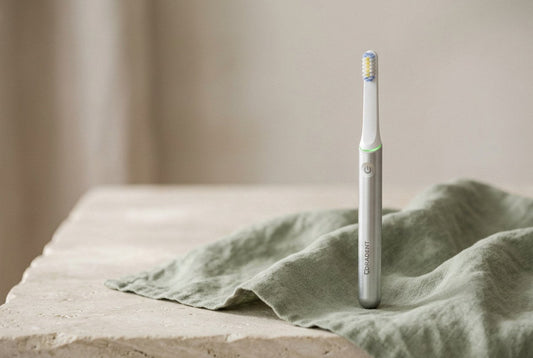 PulseONE sonic toothbrush in Platinum standing on a soft sage green linen cloth over pale stone
