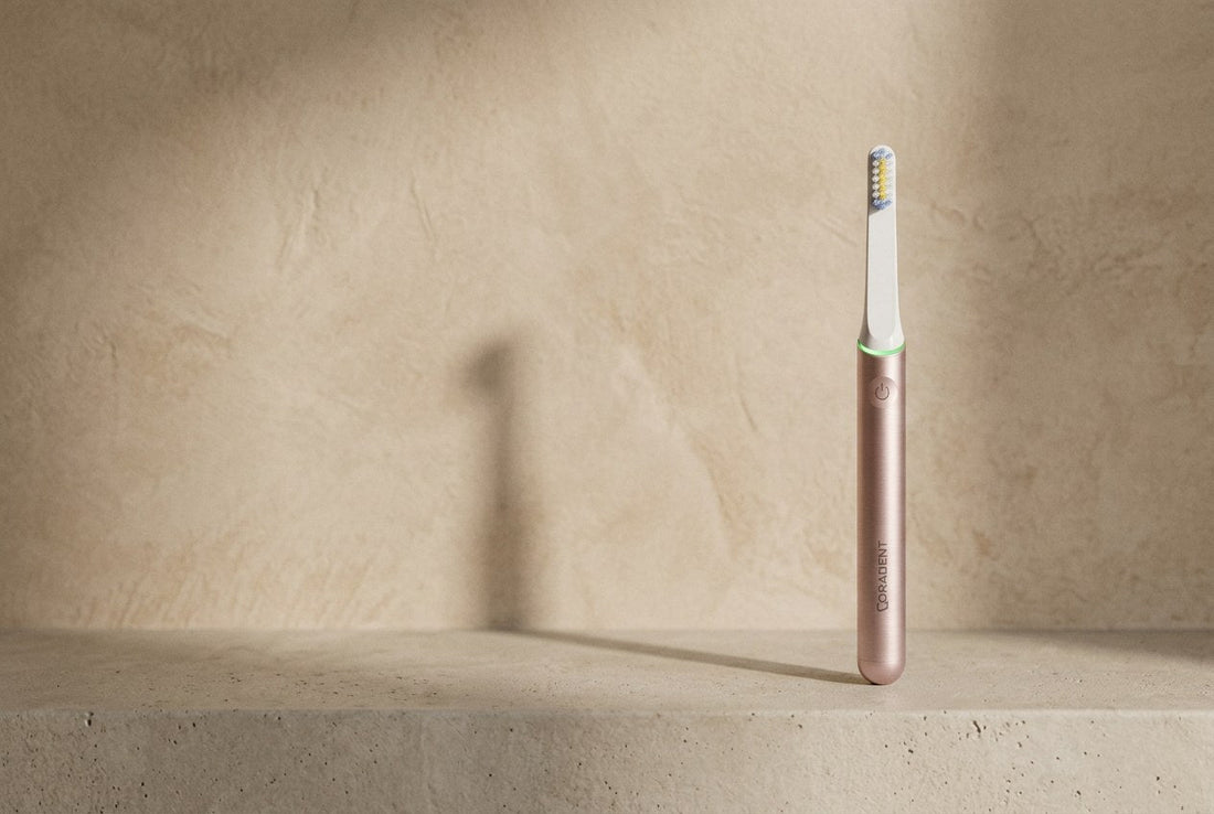 PulseONE sonic toothbrush in Rose standing on a minimal concrete ledge against a warm plaster wall